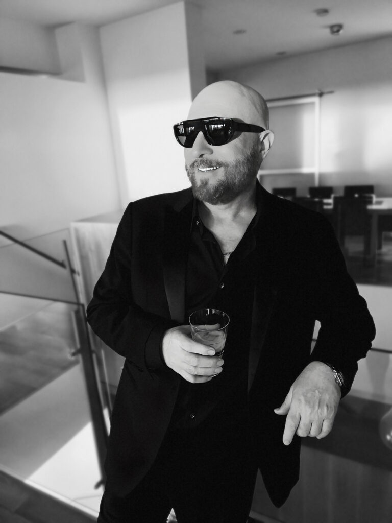 Morty Shallman holding a beverage and wearing a black suit and mirrorshades